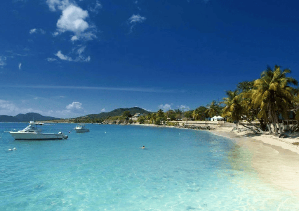 Tropical beach with clear water, boats, and palm trees under a blue sky.