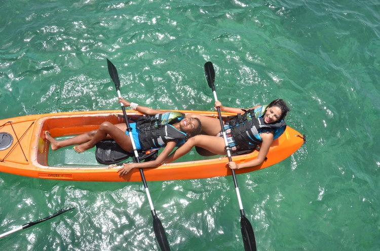 Two people relaxing in a kayak on clear green water.
