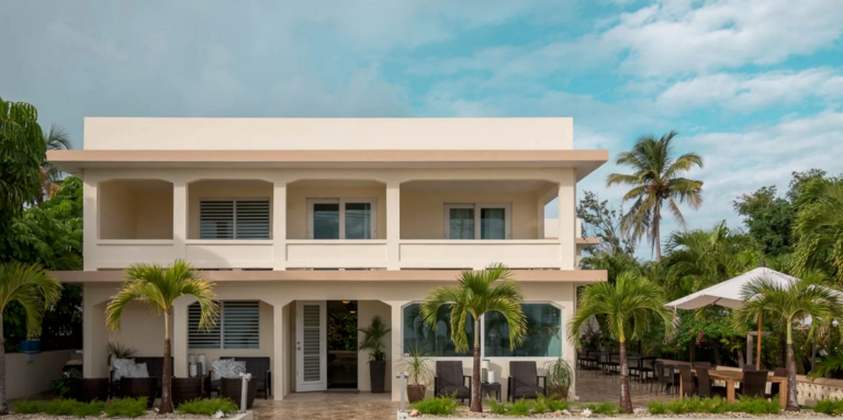 Two-story cream building with palm trees and outdoor seating area.